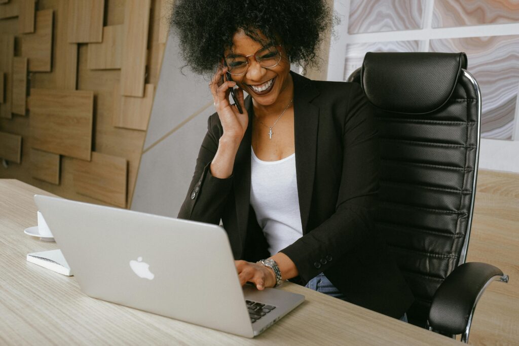 pexels-photo-3727464-3727464-1 Smiling woman on phone call while working on a laptop in a stylish office.
